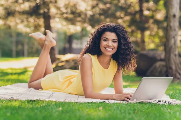 Zdjęcie dziewczyny leżał krata wpisując netbook wygląd aparat błyszczący biały uśmiech nosić żółtą sukienkę w parku na zewnątrz — Zdjęcie stockowe