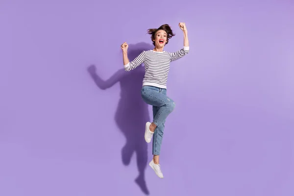 Foto de comprimento total de senhora sortuda engraçada vestida roupas casuais pulando altos punhos em ascensão isolado cor roxa fundo — Fotografia de Stock