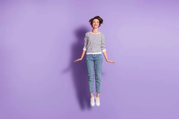 Фотографія повної довжини весела красива молода жінка носить повсякденне вбрання, стрибаючи з високим ізольованим фіолетовим кольоровим фоном — стокове фото