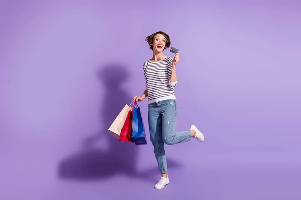 Πλήρης φωτογραφία μήκος του αξιολάτρευτο αγοραστή γυναίκα φορούν casual στολή κρατώντας πολύχρωμα τσάντες ψώνια πιστωτική κάρτα απομονωμένο βιολετί φόντο χρώμα — Φωτογραφία Αρχείου