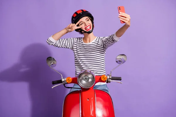 Foto von Mädchen Fahrt Moped schießen Selfie Smartphone zeigen V-Zeichen tragen Helm gestreiftes Hemd isoliert violette Farbe Hintergrund — Stockfoto
