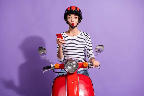 Zdjęcie szokujące pani dysk motocykl trzymać telefon komórkowy otwarte usta nosić kask paski koszula odizolowany fioletowy kolor tło — Zdjęcie stockowe