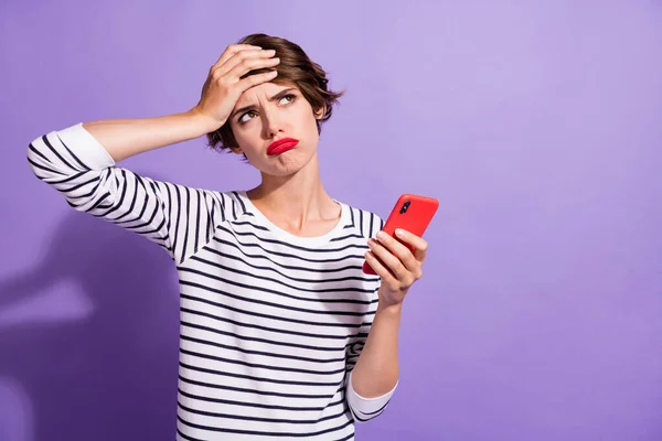 Foto van verontruste boos meisje houden mobiele telefoon palm wenkbrauw look lege ruimte dragen gestreept shirt geïsoleerde paarse kleur achtergrond — Stockfoto