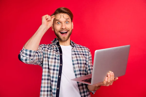 Foto von selbstbewussten aufgeregten jungen Mann tragen kariertes Hemd Armbrille hält modernes Gerät lächelnd isoliert rote Farbe Hintergrund — Stockfoto