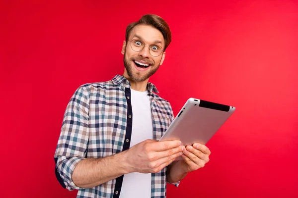 Foto de bastante dulce joven caballero vestido a cuadros gafas de camisa sosteniendo gadget moderno aislado fondo de color rojo — Foto de Stock