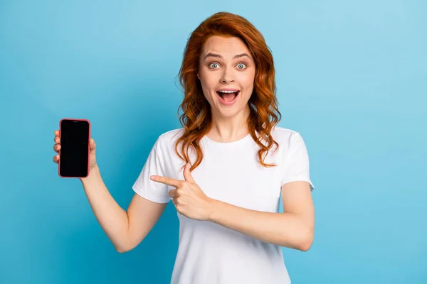 Foto retrato de menina animado apontando o dedo para o telefone com espaço de exibição em branco isolado no fundo de cor azul pastel — Fotografia de Stock