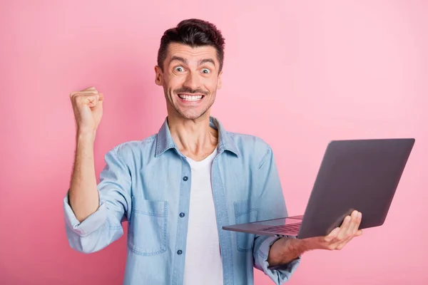 Πορτρέτο του συμπαθητικού χαρούμενου άντρα που κρατά στα χέρια χρησιμοποιώντας φορητό υπολογιστή που διασκεδάζει γιορτάζοντας απομονωμένη πάνω από ροζ παστέλ χρώμα φόντο — Φωτογραφία Αρχείου