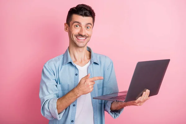 Photo portrait geek pointing finger computer smiling recommending in blue shirt isolated pastel pink color background — Stock Photo, Image