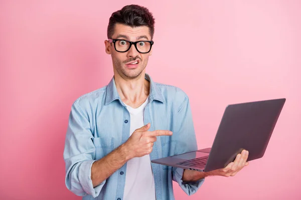 Portret miłego sceptycznego faceta trzymającego w dłoniach laptop wskazujący ekran wyizolowany nad różowym pastelowym tłem koloru — Zdjęcie stockowe