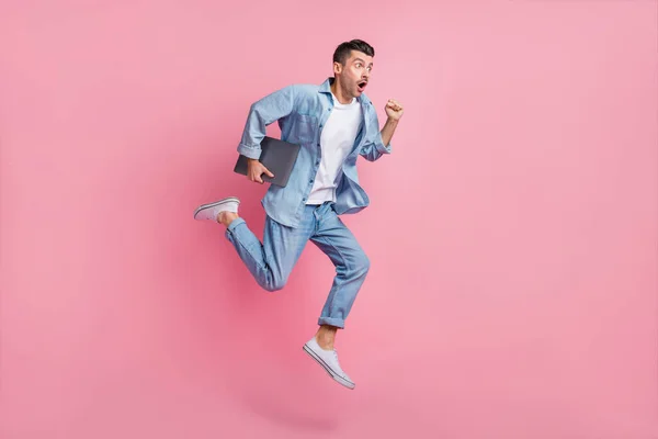Lunghezza completa dimensione del corpo vista di bel ragazzo motivato energico saltare portando laptop in esecuzione veloce isolato su sfondo rosa pastello — Foto Stock