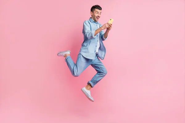 Volledige lichaamsomvang uitzicht van mooie vrolijke verslaafde gerichte man met behulp van gadget geïsoleerd over roze pastel kleur achtergrond — Stockfoto