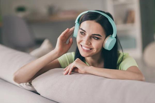 Foto de niña alegre sentarse sofá sonrisa blanca inspirada mirada escuchar música usar auriculares camiseta verde en el interior — Foto de Stock