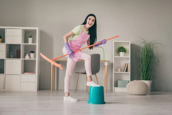 Comprimento total do corpo tamanho vista de muito alegre engraçado menina de cabelos compridos empregada doméstica usando esfregão como guitarra se divertindo na luz interior quarto — Fotografia de Stock