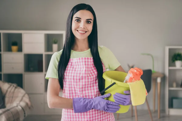 Retrato de menina de cabelos longos alegre atraente segurando em balde de mãos com suprimentos de limpeza na sala de estar interior leve — Fotografia de Stock