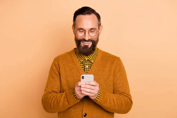 Photo de l'homme joyeux tenir téléphone regarder écran porter des lunettes brun cardigan isolé couleur beige fond — Photo