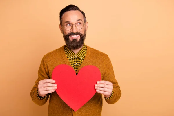 Foto di romantico uomo tenere il cuore rosso figura guardare vuoto spazio usura specifiche marrone cardigan isolato colore beige sfondo — Foto Stock