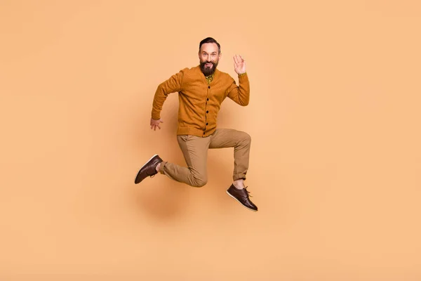 Full Size Profilfoto von optimistischen braunen Haaren Mann Sprung tragen braunen Pullover Hose Schuhe isoliert auf beige Farbhintergrund — Stockfoto