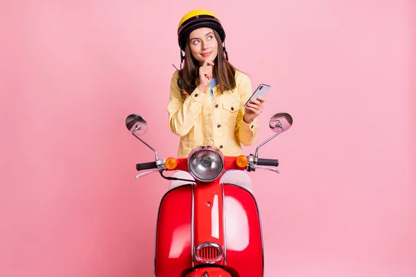 Foto de jovem sonhador atraente menina olhar copyspace desgaste amarelo capacete passeio vermelho moto segurar telefone isolado no fundo cor-de-rosa — Fotografia de Stock