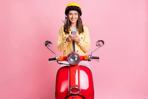 Foto de jovem sorrindo positivo menina mulher conversando telefone desgaste amarelo capacete passeio moto vermelha isolada no fundo cor-de-rosa — Fotografia de Stock