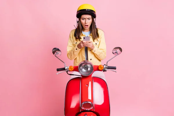 Foto de jovem chocado atraente menina mulher ler sms no telefone desgaste amarelo capacete passeio moto vermelha isolada no fundo cor-de-rosa — Fotografia de Stock