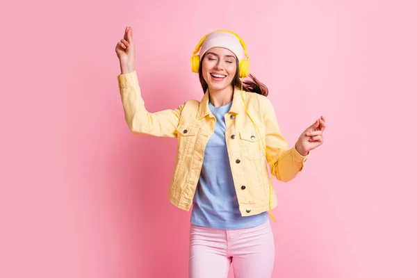 Zdjęcie uroczej optymistycznej dziewczyny słuchać muzyki taniec nosić czapka słuchawki żółty płaszcz niebieski koszula spodnie izolowane na różowy kolor tła — Zdjęcie stockowe
