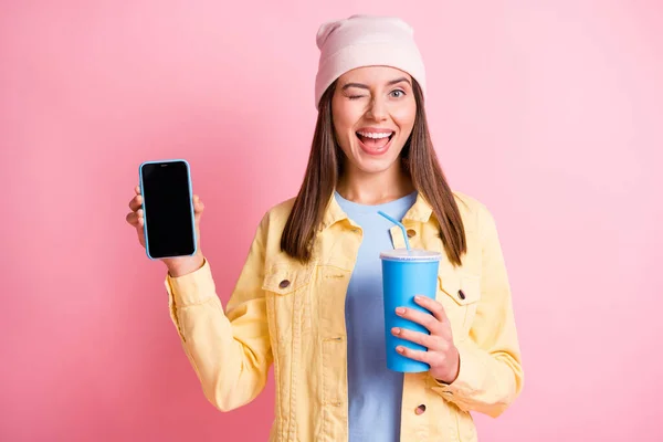 Retrato de pessoa atraente segurar bebida demonstrar telefone olho piscadela cabeça cap isolado no fundo cor-de-rosa — Fotografia de Stock