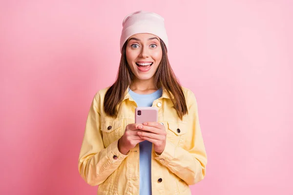 Foto de atraente animado jovem mulher usar chapéu rosa segurar telefone mensagem novidade isolado no fundo de cor brilhante — Fotografia de Stock