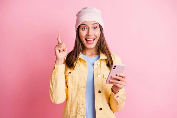 Foto de menina feliz inteligente ideia surpreso post espera smartphone ponto dedo desgaste casaco amarelo isolado no fundo cor-de-rosa — Fotografia de Stock