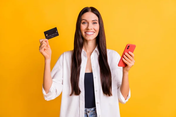 Porträtt av glada vänliga dam hålla betalkort telefon toothy leende isolerad på gul färg bakgrund — Stockfoto