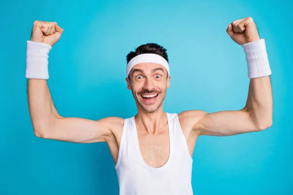 Foto de morena feliz hombre levantar los puños celebrar ganar desgaste ropa deportiva diadema aislado sobre fondo de color azul — Foto de Stock