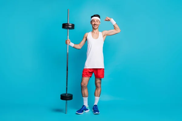 Full size photo of young sportsman happy smile proud show muscles barbell exercise wear wristband isolated over blue color background — Stock Photo, Image