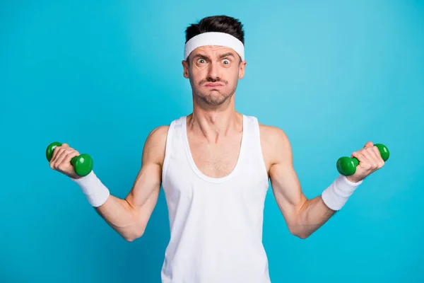 Foto des jungen Sportlers Übung mit schweren Hanteln schmollte Wangenknochen Grimassen isoliert über blauem Hintergrund — Stockfoto