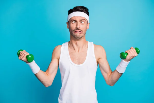 Foto de un joven deportista entrenar ejercicio con pesadas mancuernas muecas ojos se ven de manera diferente aislado sobre fondo de color azul — Foto de Stock