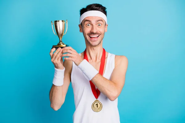 Foto de joven hombre deportivo alegre sonrisa positiva feliz ganar la competencia mantener trofeo aislado sobre fondo de color azul —  Fotos de Stock