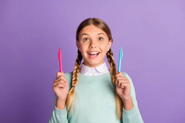Retrato fotográfico de una chica sorprendida sosteniendo dos bolígrafos en manos aisladas sobre un fondo de color púrpura vivo —  Fotos de Stock
