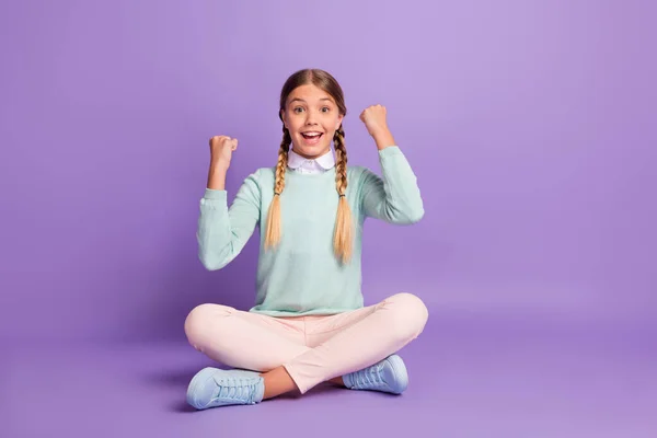 Foto de la pequeña dama alegre sentarse piso levantar los puños boca abierta usar pantalones de jersey verde zapatos aislados fondo púrpura — Foto de Stock