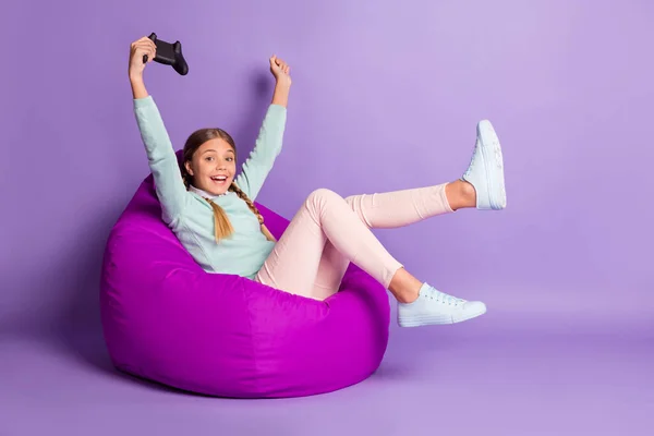 Foto de pequena senhora animada sentar beanbag segurar gamepad usar calças de camisola verde sapatos isolado fundo violeta — Fotografia de Stock