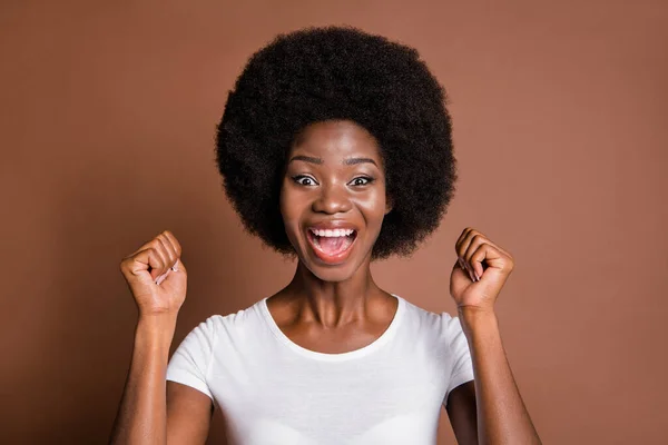 Portret van verbaasd positieve donkere huid dame vuisten omhoog open mond vieren geïsoleerd op bruine kleur achtergrond — Stockfoto