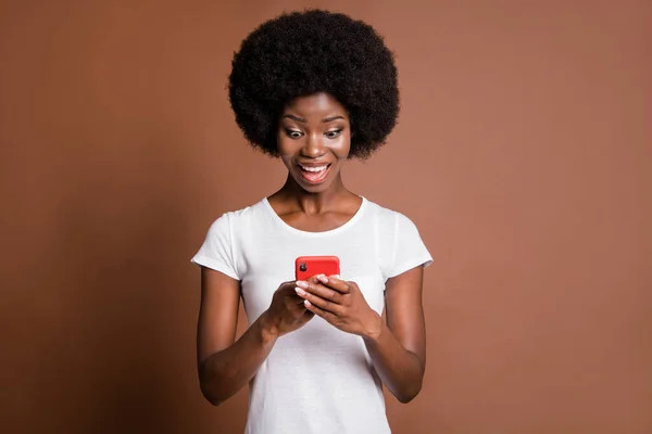 Foto van verbaasd donkere huid meisje enthousiast kijken telefoon nieuwe abonneren commentaar geïsoleerd op bruine kleur achtergrond — Stockfoto