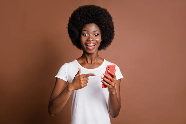 Portret van verbaasd aantrekkelijke donkere huid persoon geven vinger telefoon geïsoleerd op bruine kleur achtergrond — Stockfoto