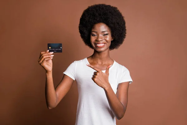 Foto retrato de mujer mostrando crédito bancario dedo sonriendo en traje casual aislado sobre fondo de color marrón — Foto de Stock