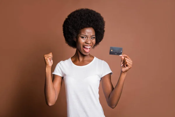 Portret van verbaasd donkere huid meisje hand houden debetkaart open mond schreeuwen vuist omhoog geïsoleerd op bruine kleur achtergrond — Stockfoto