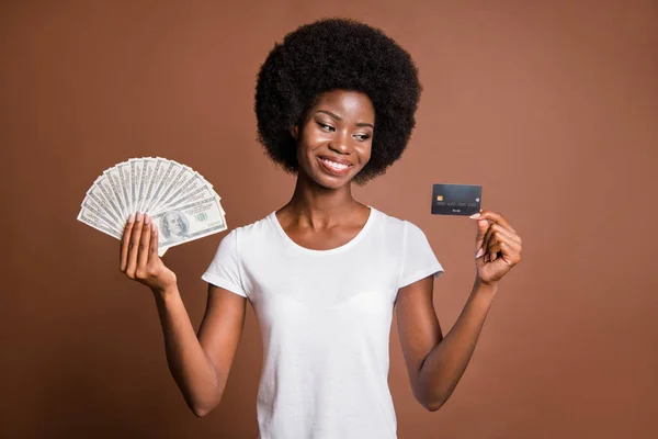 Portret kobiety patrzącej na kartę kredytową trzymającej banknoty dolary pensja odizolowana na brązowym tle — Zdjęcie stockowe