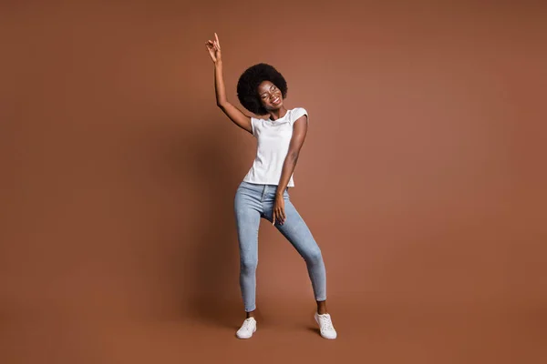 Foto di allegra danza ragazza africana sollevare mano indossare bianco t-shirt jeans jeans calzature isolato colore marrone sfondo — Foto Stock