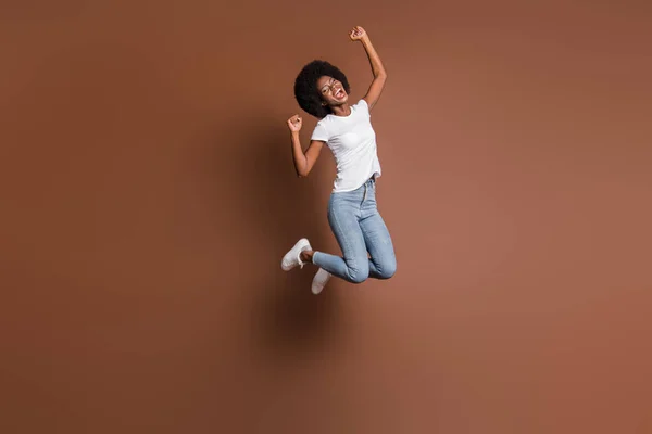 Lungimea completă a corpului fotografie de fată sărind gesturi înalte ca câștigător fericit izolat pe fundal de culoare maro — Fotografie, imagine de stoc