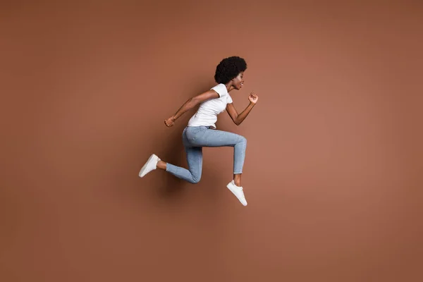 スポーティな女の子のジャンプランのプロフィール写真は、白いTシャツのジーンズの履物孤立茶色の色の背景を着用 — ストック写真