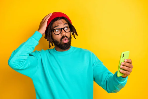 Retrato de morena chico impresionado mantenga teléfono desgaste gorra gafas jersey azul aislado sobre fondo de color vivo amarillo —  Fotos de Stock