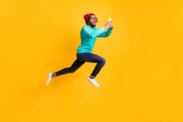 Foto de perfil em tamanho completo de morena otimista cara pular correr tirar foto desgaste óculos pulôver jeans isolado no fundo amarelo — Fotografia de Stock