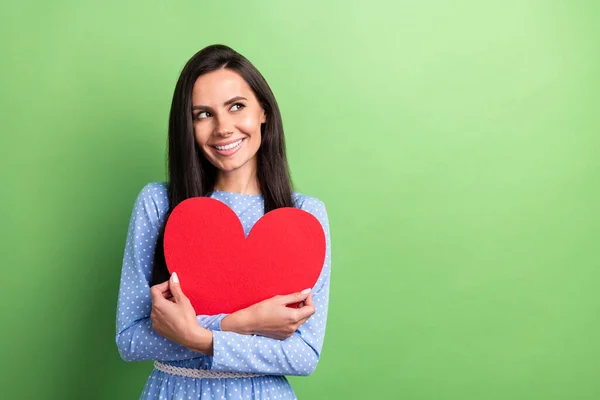 Foto de sonho muito jovem senhora usar roupas pontilhadas sorrindo abraçando coração vermelho olhando espaço vazio isolado cor verde fundo — Fotografia de Stock