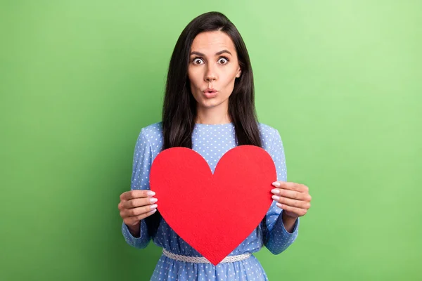 Photo de femme aux cheveux bruns impressionnée tenir papier coeur porter robe bleue isolé sur fond de couleur verte — Photo